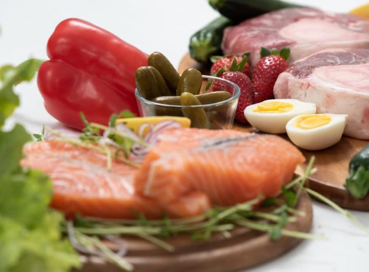 A vibrant assortment of fresh salmon, eggs, vegetables, and fruits arranged on a wooden platter.