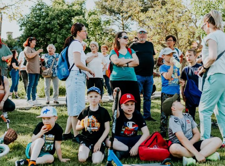 A diverse group of families and children enjoying an outdoor event on a sunny day in a park setting.